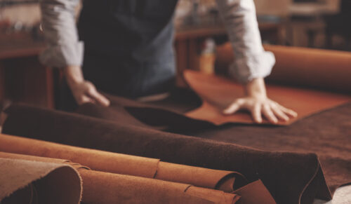 Man shoemaker hold different rolls natural leather brown, working with textile in workshop.